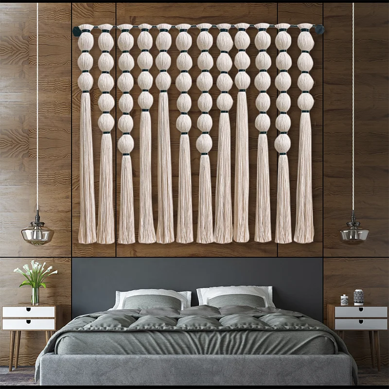 Large beaded macramé wall hanging in neutral tones above bed